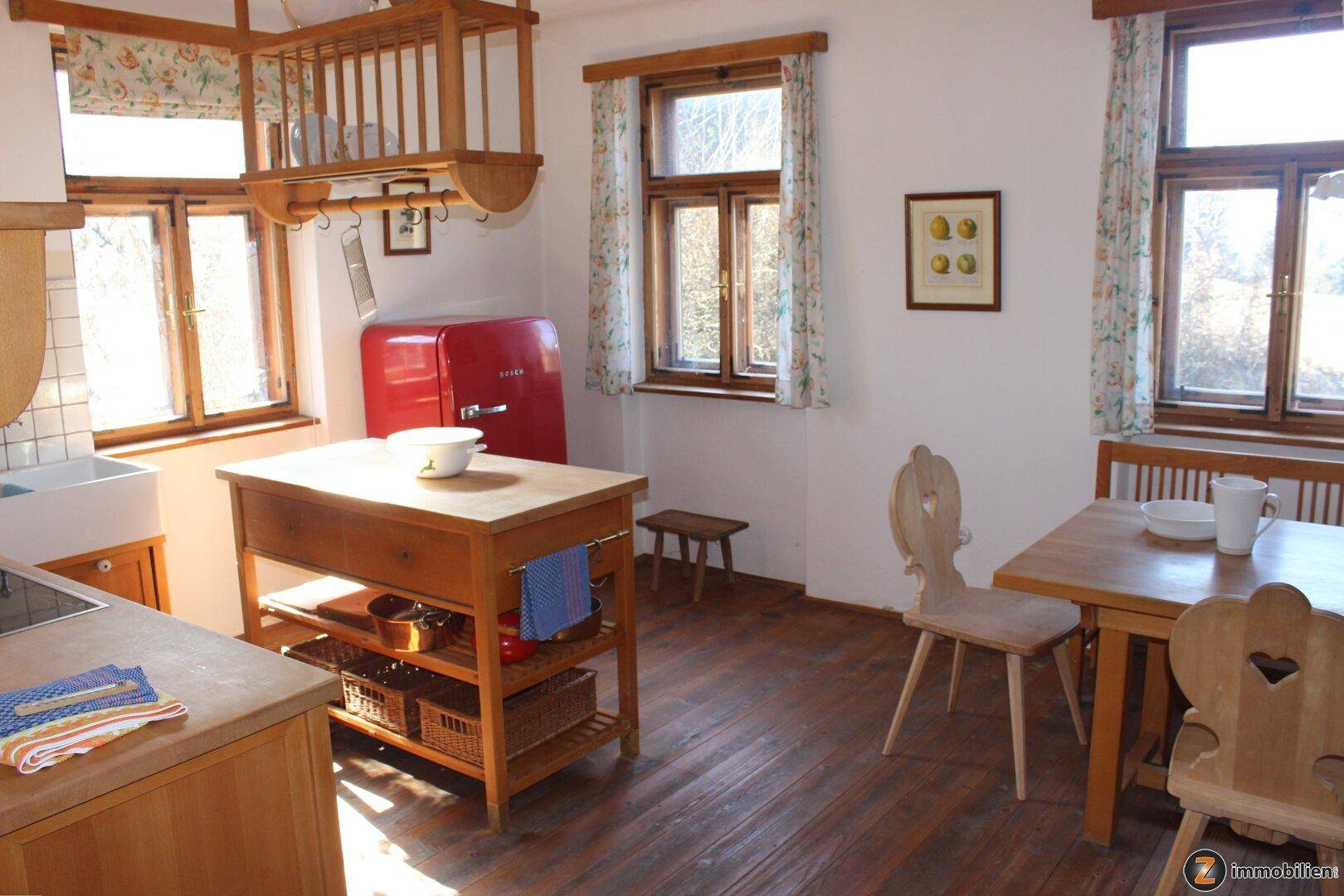 Helle Küche mit Holzboden, rotem Kühlschrank und Blick ins Grüne durch die Fenster.