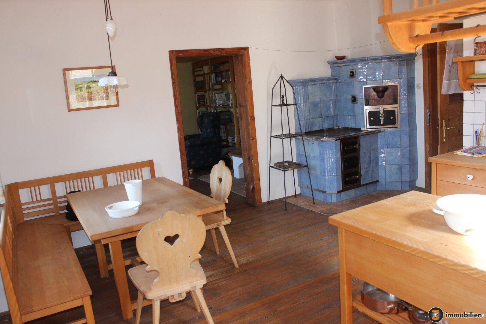 Rustikale Wohnküche mit Holztisch, Eckbank und einem traditionellen Kachelofen.