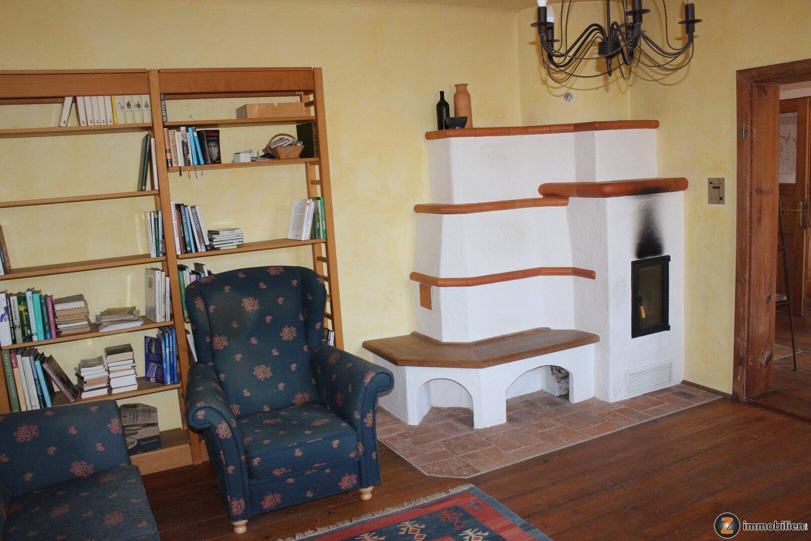 Gemütliches Wohnzimmer mit Kachelofen, Holzboden und einem Bücherregal.
