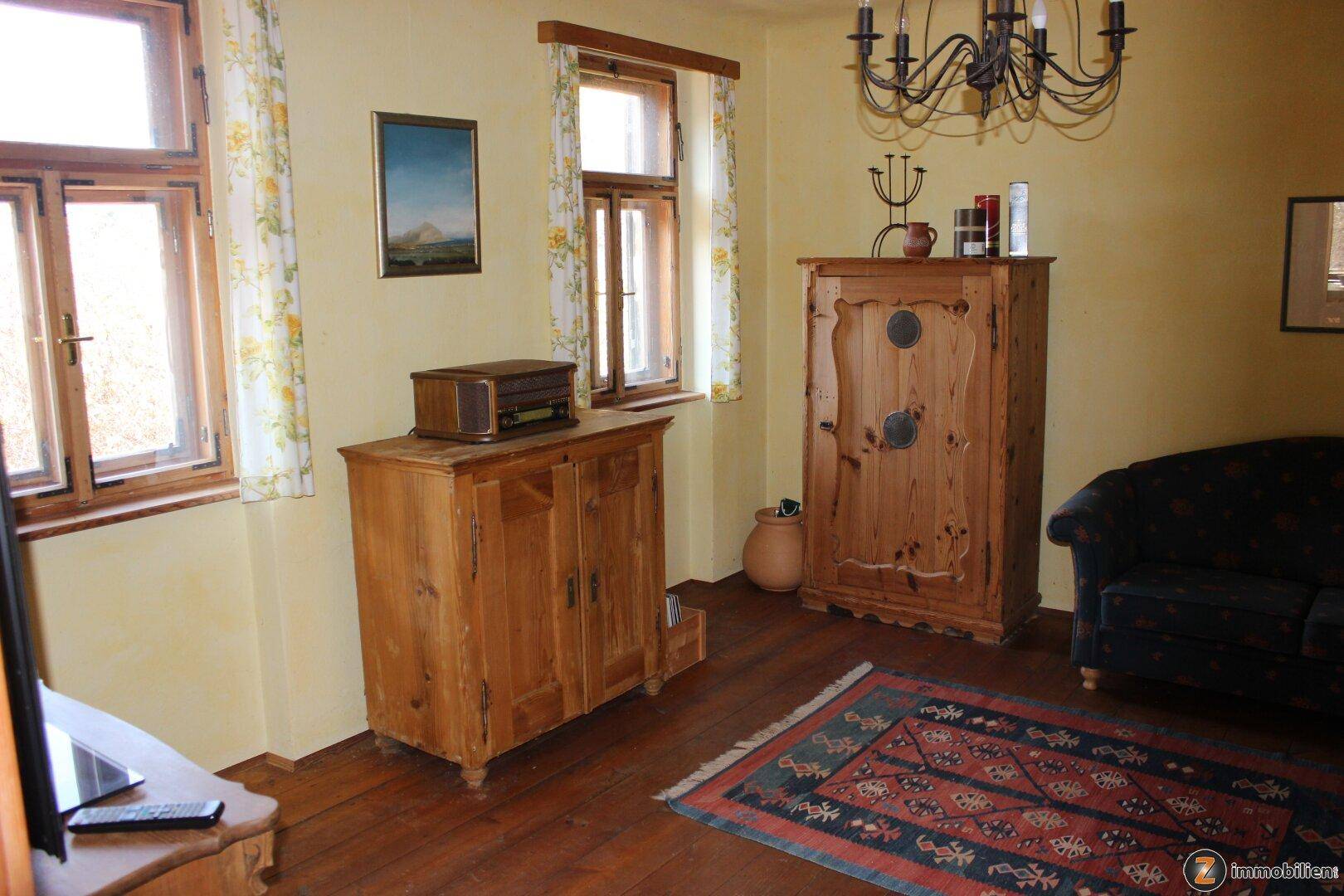 Wohnzimmer im Landhausstil mit Holzmöbeln, Teppich und Blick nach draußen.