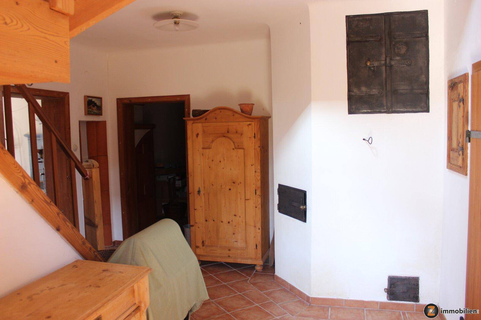 Eingangsbereich mit Terrakottafliesen, Holztreppe und rustikalem Holzschrank.