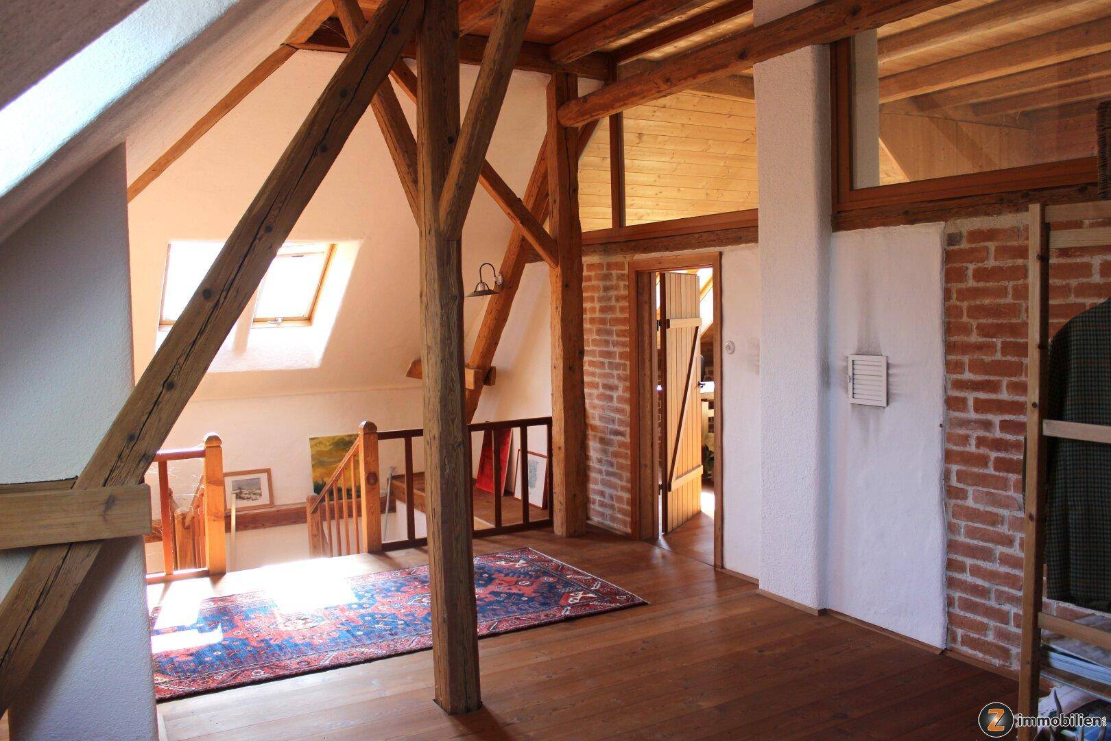 Heller Dachbodenbereich mit sichtbaren Holzbalken, Holzboden und Dachfenstern.