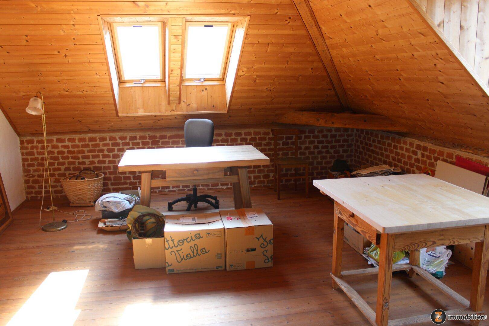 Dachgeschosszimmer mit Holzboden, Holzwänden und zwei großen Schreibtischen.