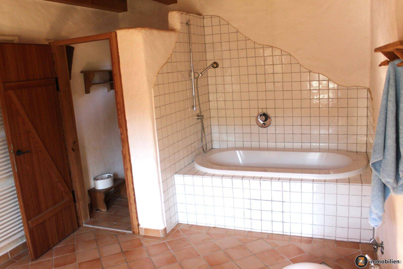 Badezimmer mit eingebauter Badewanne, weißen Fliesen und Terrakotta-Boden.