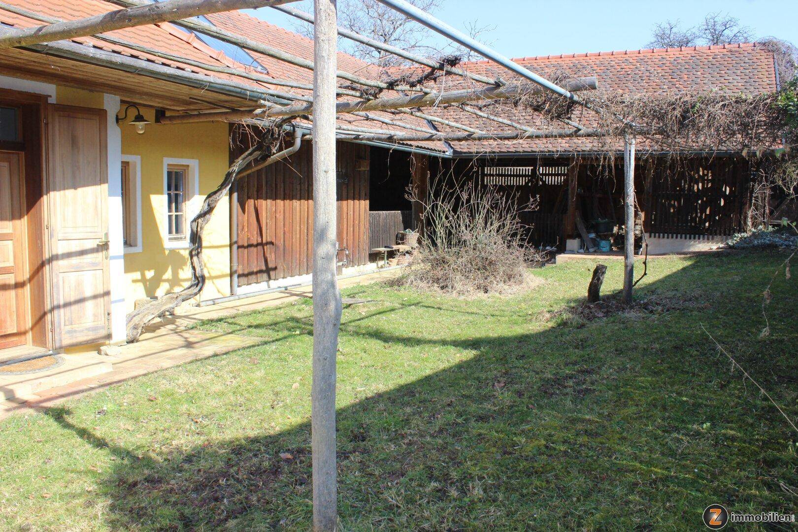 Grüner Gartenbereich mit einer Pergola und Blick auf das Nebengebäude.