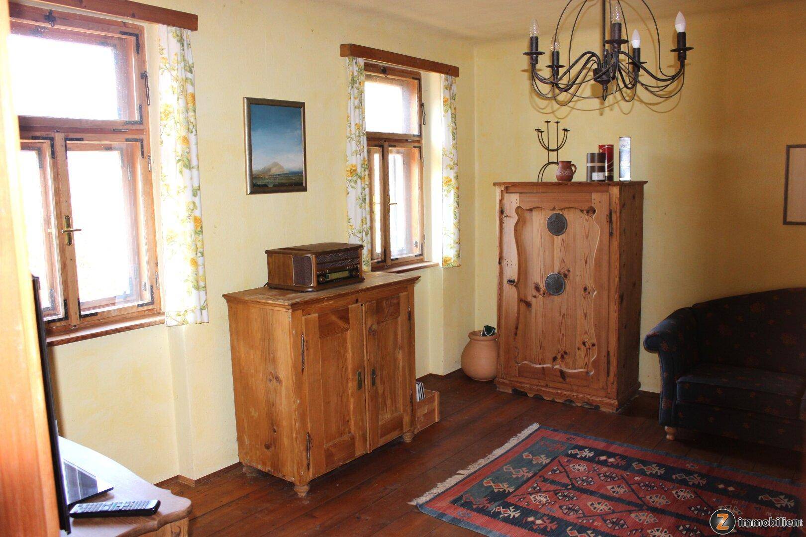 Wohnzimmer im Landhausstil mit Holzmöbeln, Teppich und Blick nach draußen.
