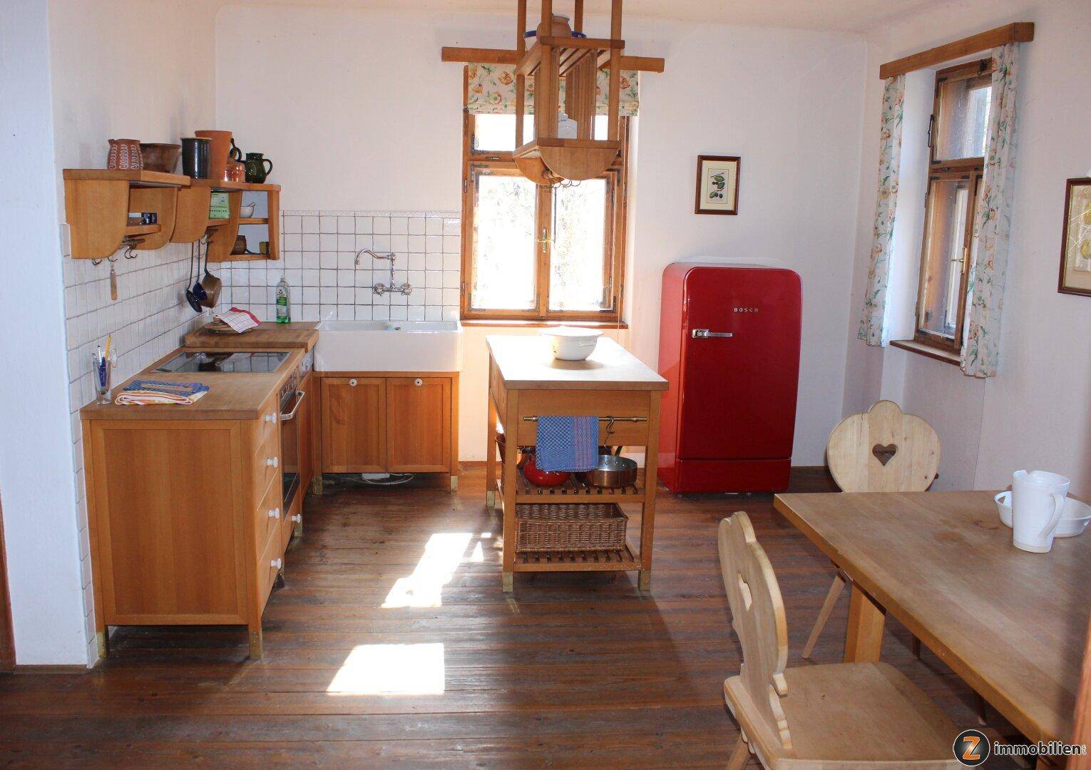 Helle Küche mit Holzboden, rotem Kühlschrank und Blick ins Grüne durch die Fenster.