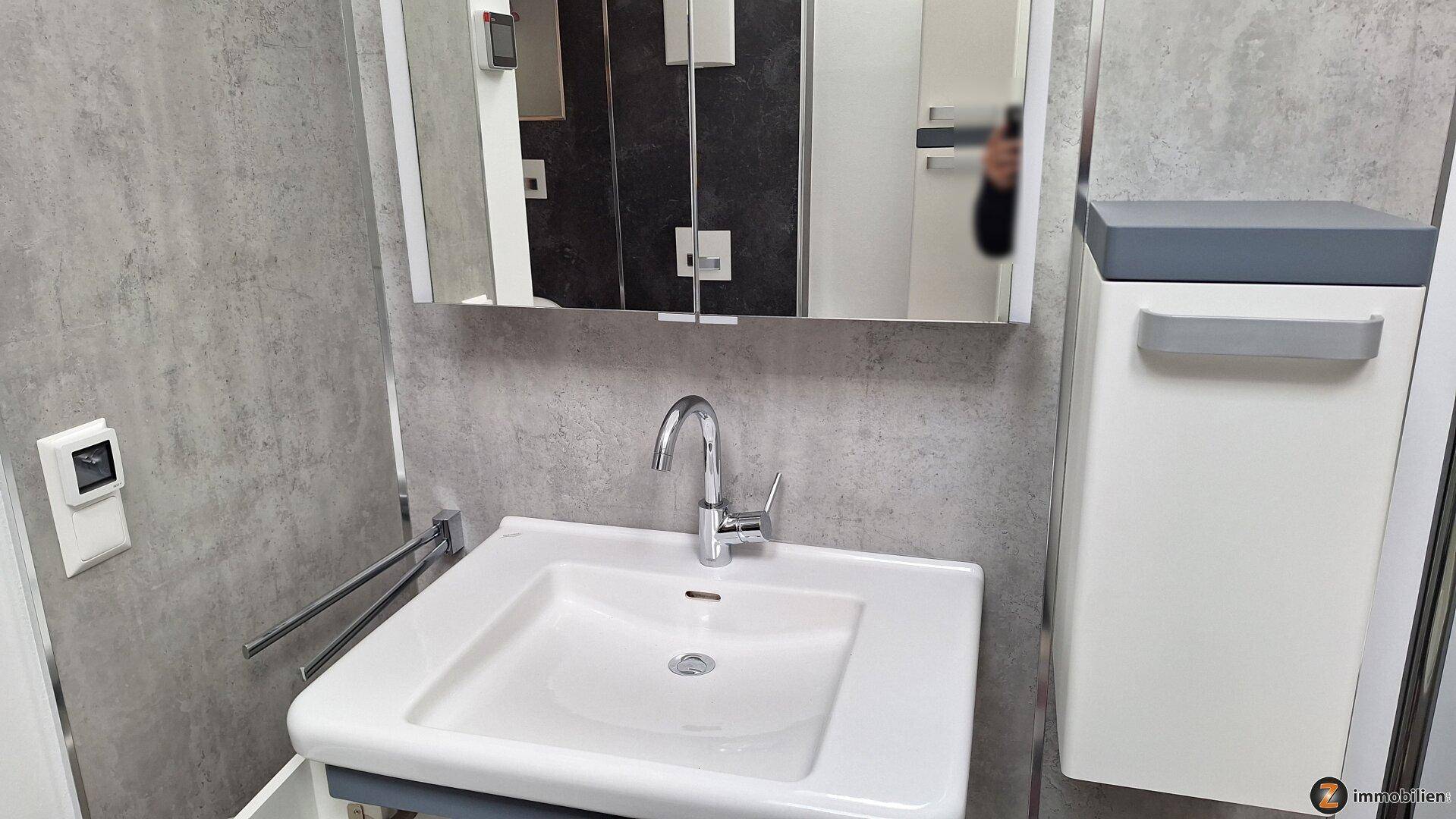 Waschbecken mit modernem Wasserhahn, Spiegelschrank und grauen Wandfliesen im Badezimmer.