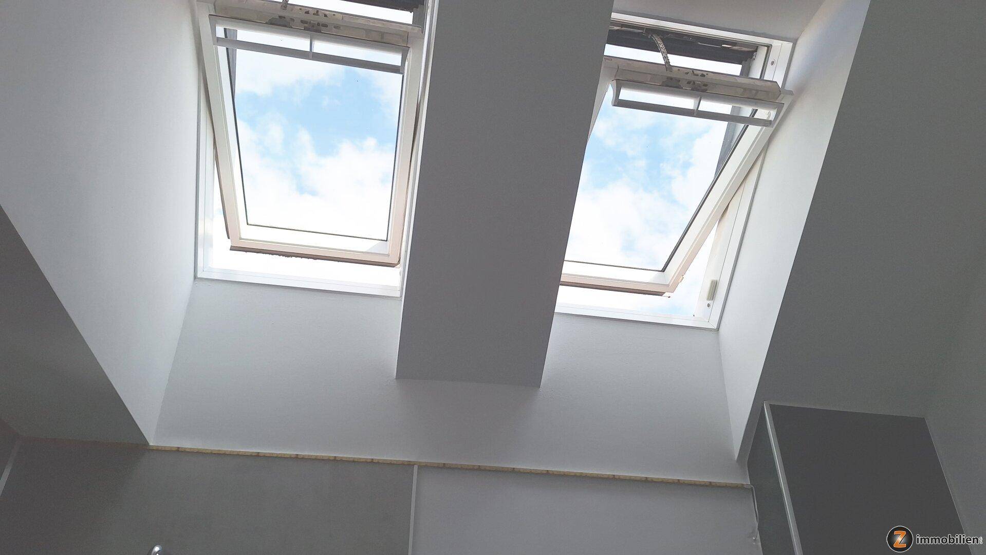 Zwei Dachfenster lassen viel Tageslicht in den Raum, mit Blick auf den blauen Himmel.