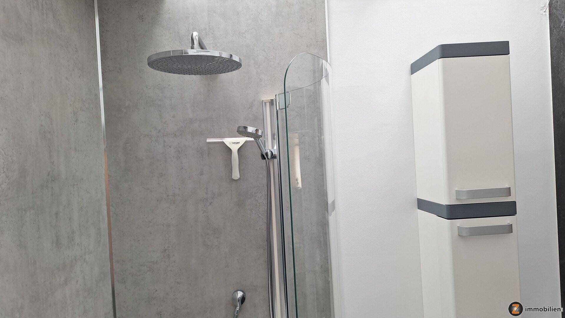 Regendusche mit Glasabtrennung und grauen Wandfliesen in einem modernen Badezimmer.