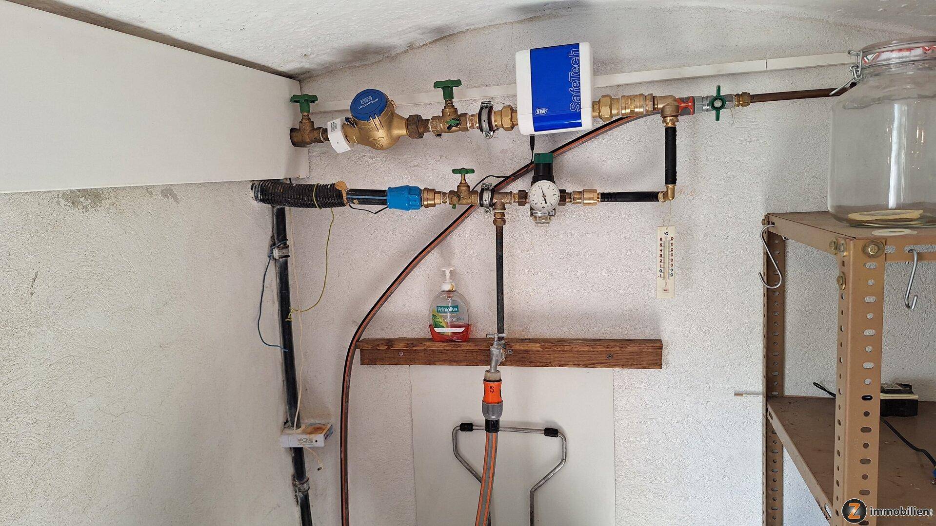 Versorgungsleitungen und Wasserzähler in einem Hauswirtschaftsraum oder Kellerbereich.