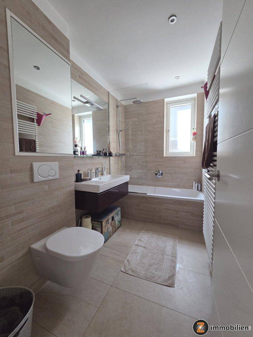 Helles Badezimmer mit Badewanne, Dusche, Fenster und modernem Waschtisch.