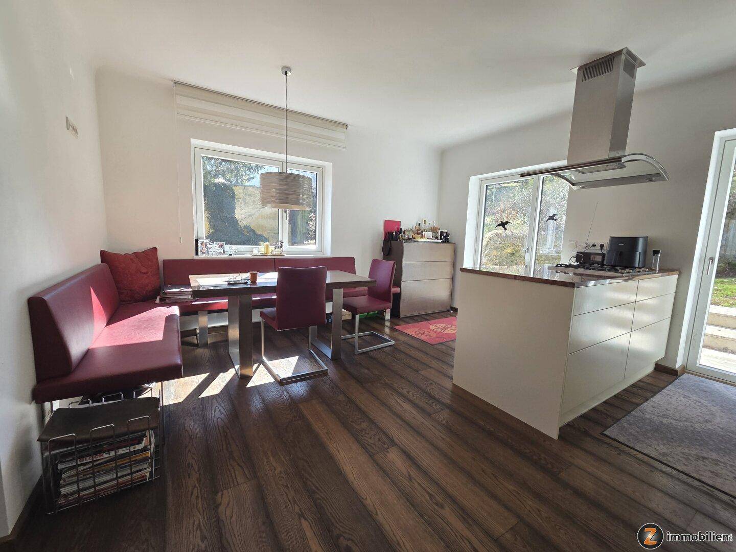 Moderne Wohnküche mit dunklem Holzboden, Kücheninsel und gemütlicher Essecke am Fenster.