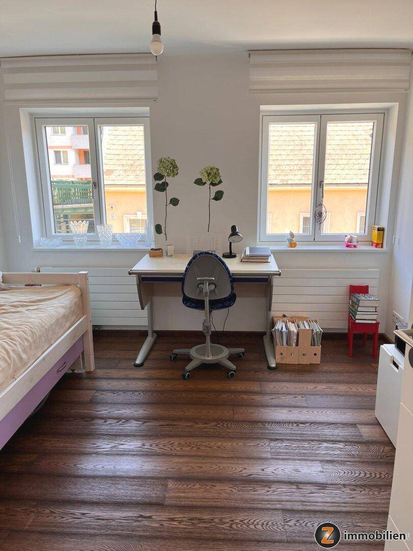 Kinderzimmer oder Arbeitszimmer mit zwei Fenstern, Schreibtisch und Holzboden.
