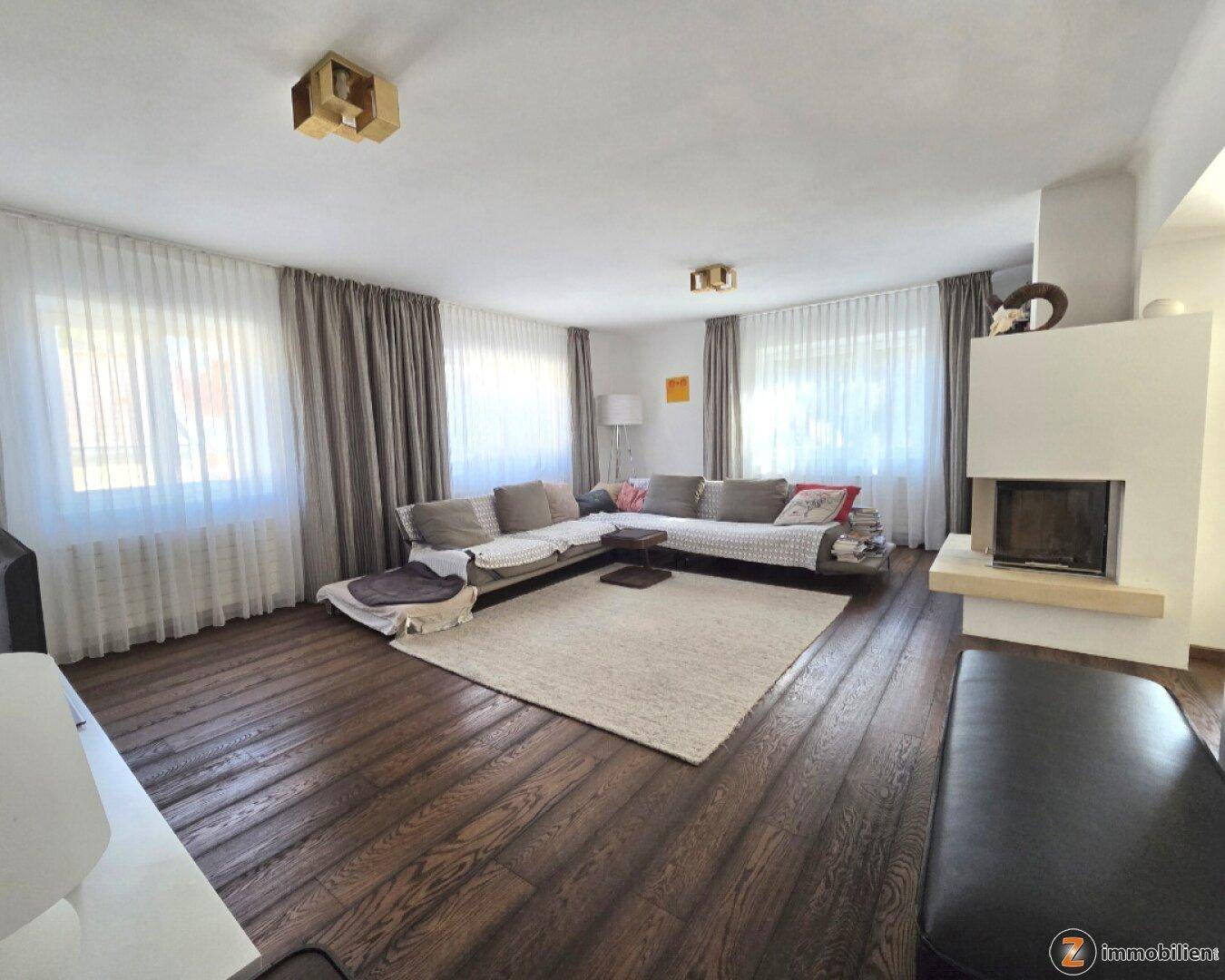 Geräumiges Wohnzimmer mit großem Sofa, dunklem Holzboden und modernem Kamin für gemütliche Abende.