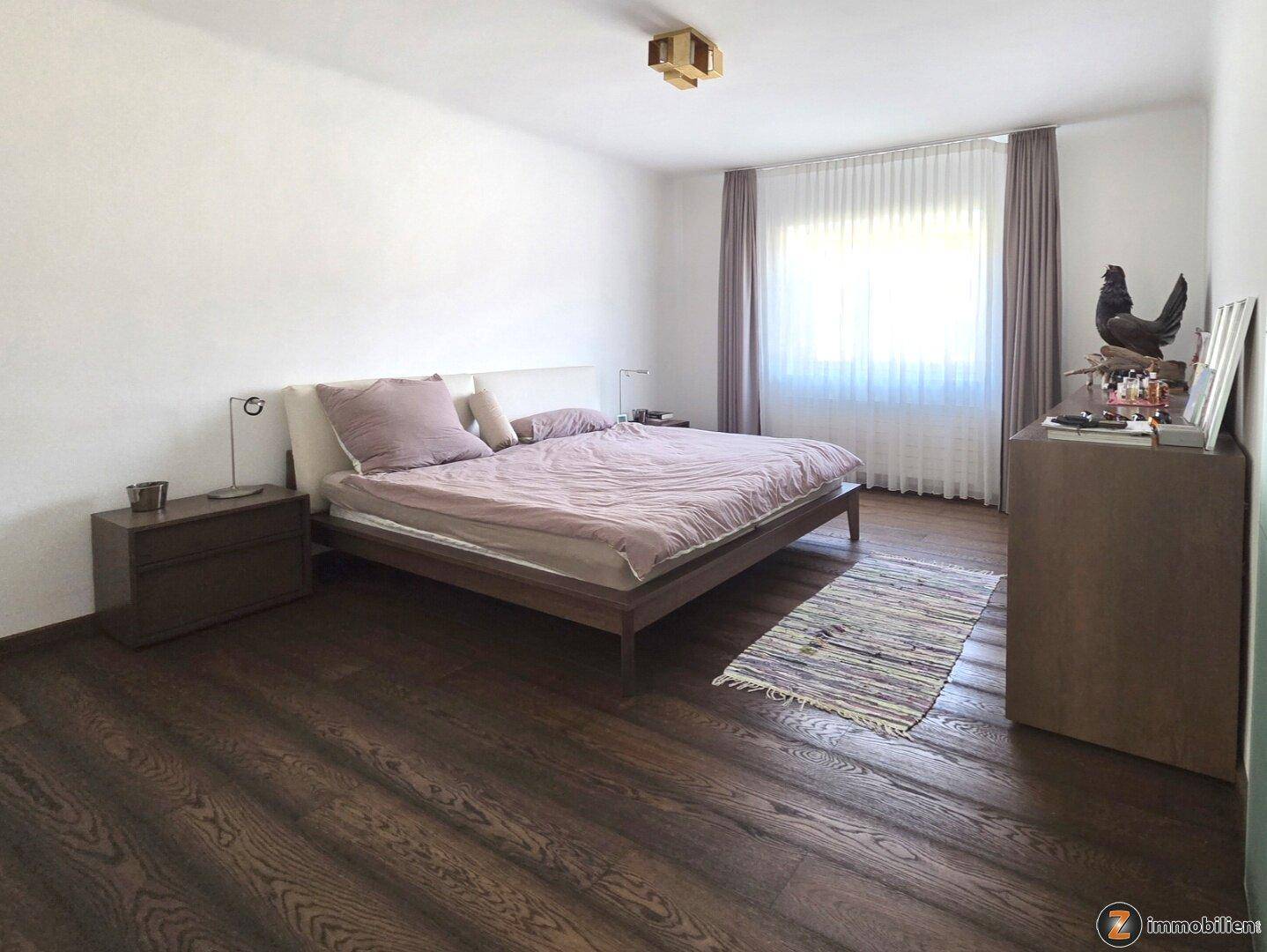 Geräumiges Schlafzimmer mit Doppelbett, dunklem Holzboden und großem Fenster.