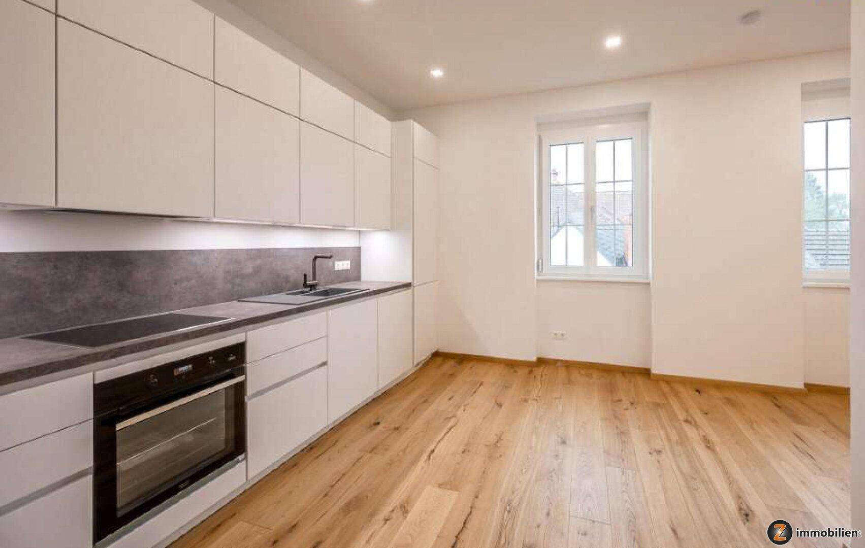 Moderne, helle Küche mit weißen Schränken, Holzboden und integrierten Geräten.