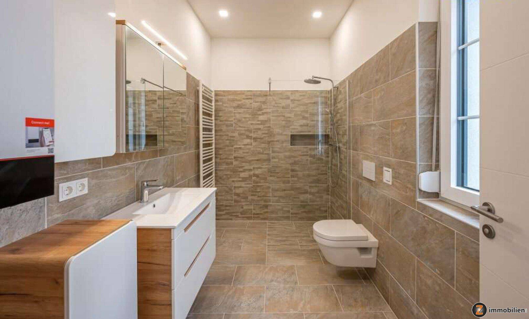 Modernes Badezimmer mit großen Fliesen, begehbarer Dusche und wandhängendem WC.