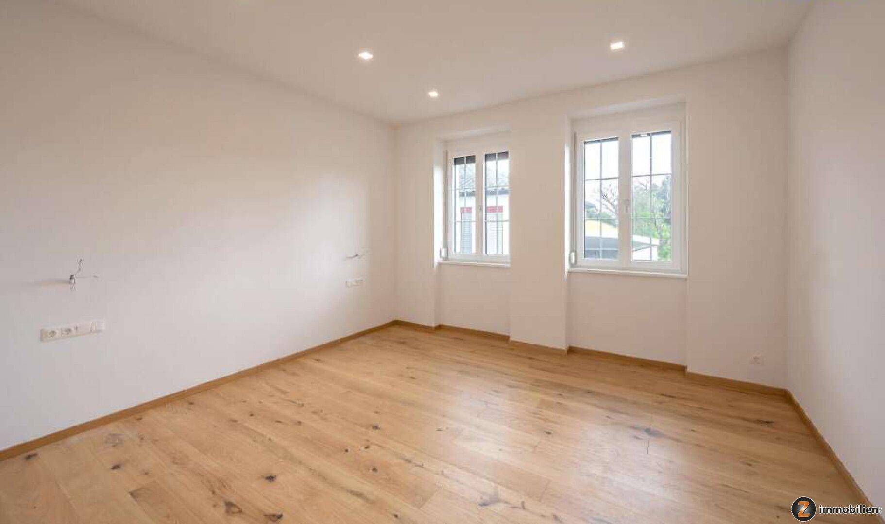 Geräumiges, helles Zimmer mit zwei Fenstern und Holzboden, ideal als Schlafzimmer.
