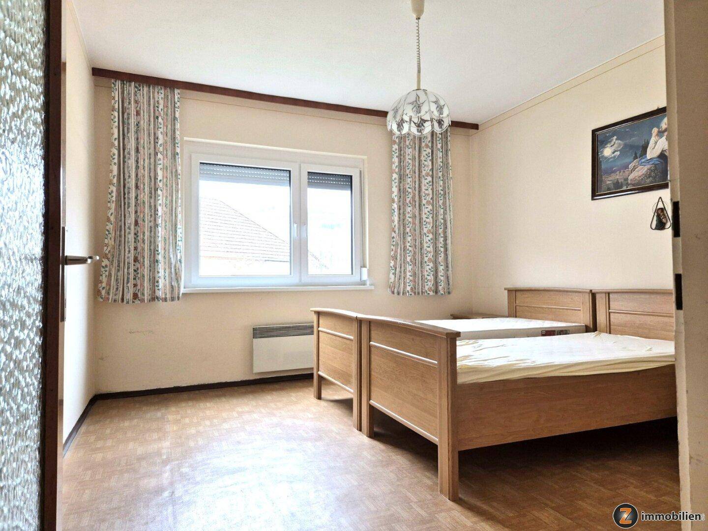 Schlafzimmer mit zwei Einzelbetten, Parkettboden und einem Fenster mit Blick nach draußen.