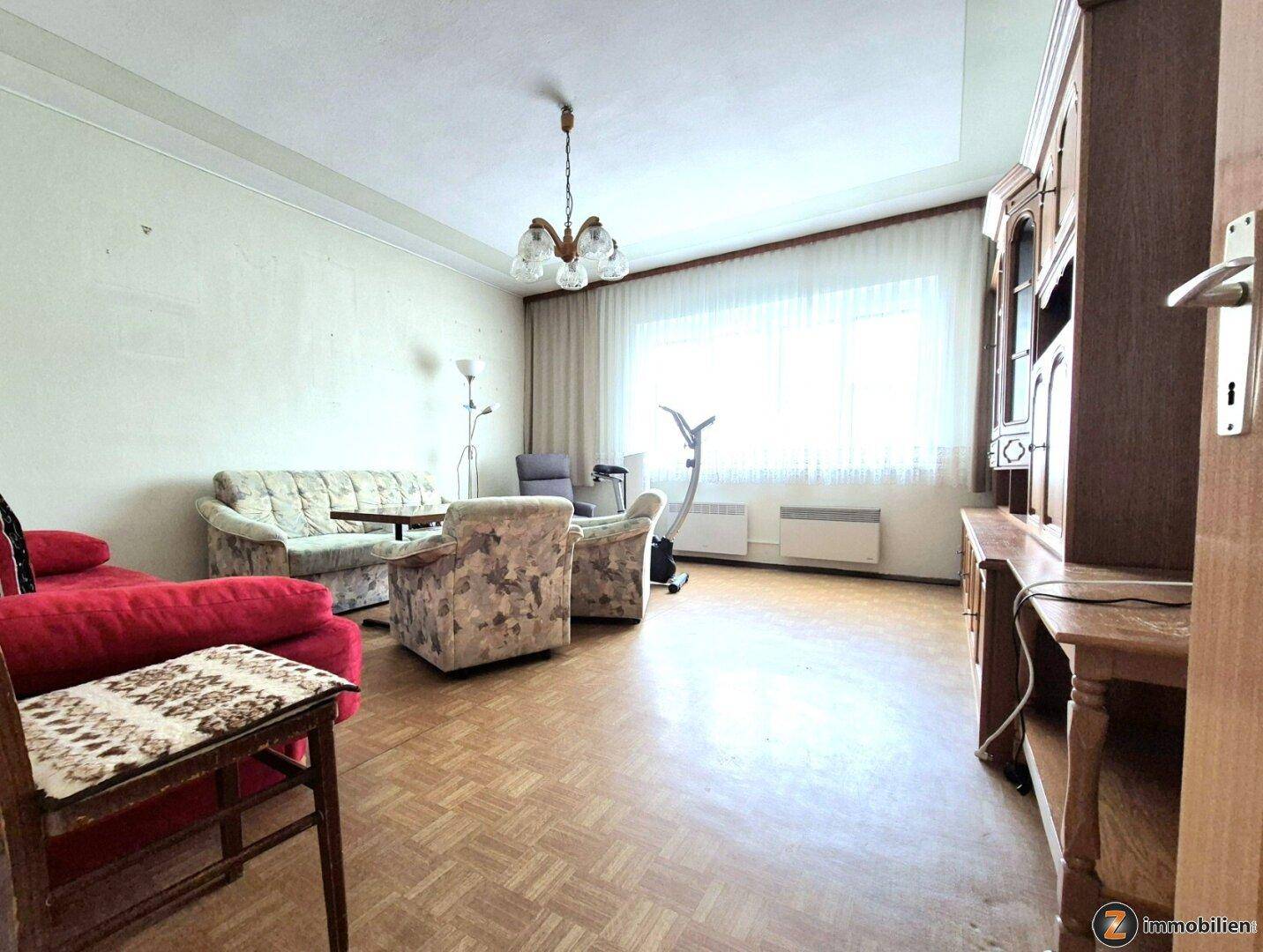 Gemütliches Wohnzimmer mit Sitzmöbeln, Parkettboden und großem Fenster für viel Licht.