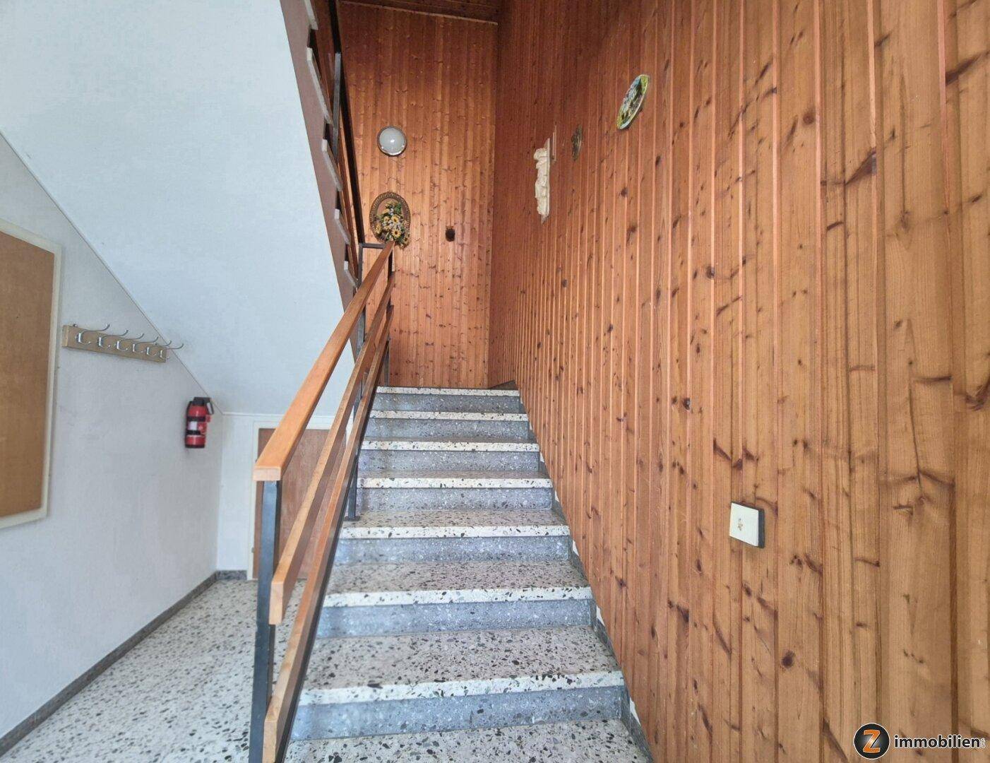 Treppenhaus mit Holzvertäfelung und Terrazzostufen, das die Stockwerke verbindet.