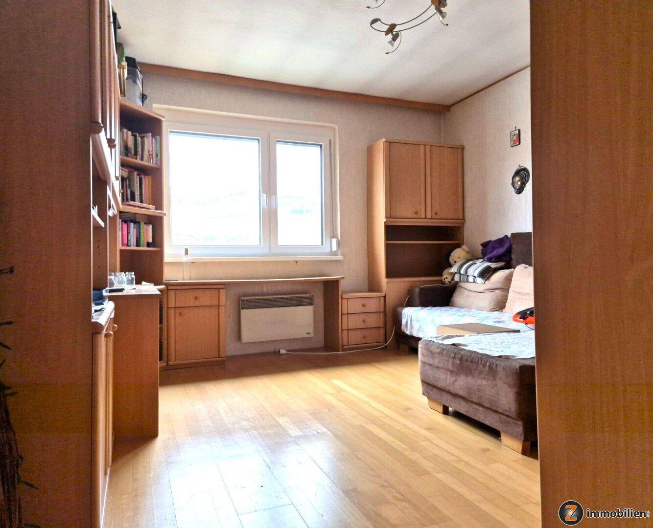 Arbeitszimmer mit Holzmöbeln, Bücherregal und Fenster, das den Raum erhellt.