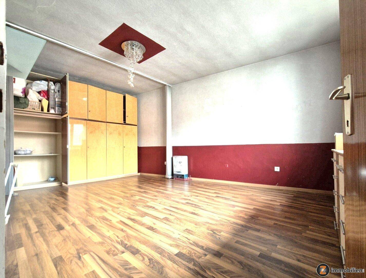 Geräumiges Zimmer mit Holzboden, Einbauschränken und dekorativer Deckenleuchte.
