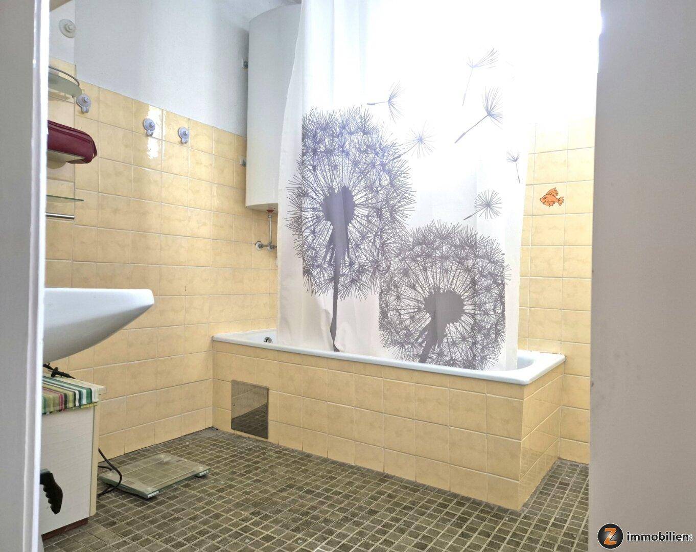 Badezimmer mit Badewanne, Waschbecken und gelben Fliesen, ausgestattet mit Duschvorhang.