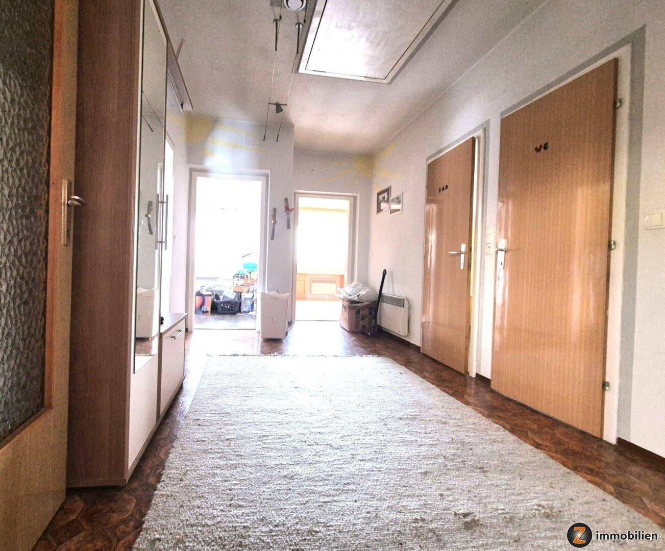 Heller Flur mit Teppichläufer, Holzschrank und Zugang zu verschiedenen Räumen.
