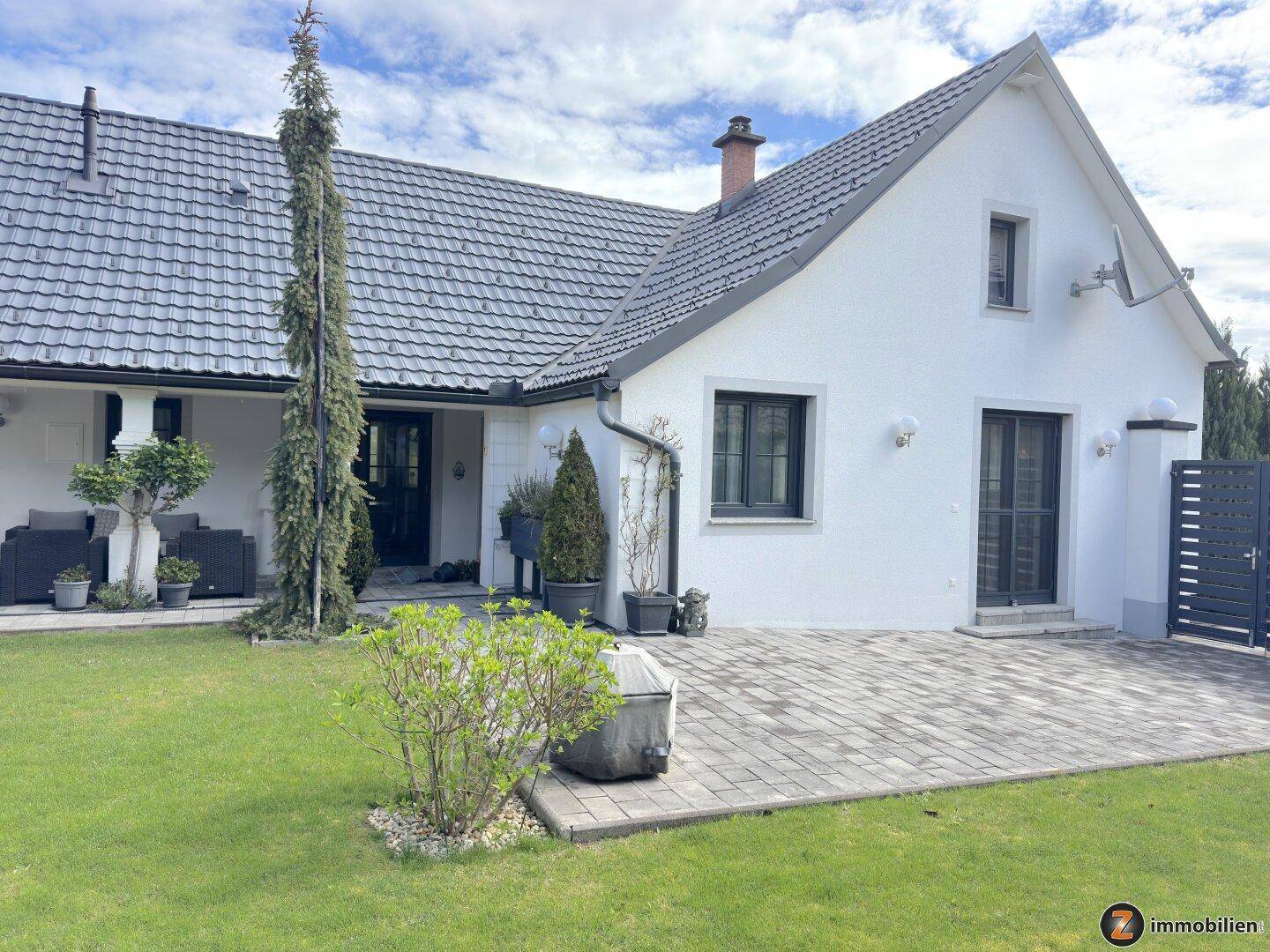 Seitenansicht des Hauses mit gepflasterter Fläche und Zugang zum Garten.