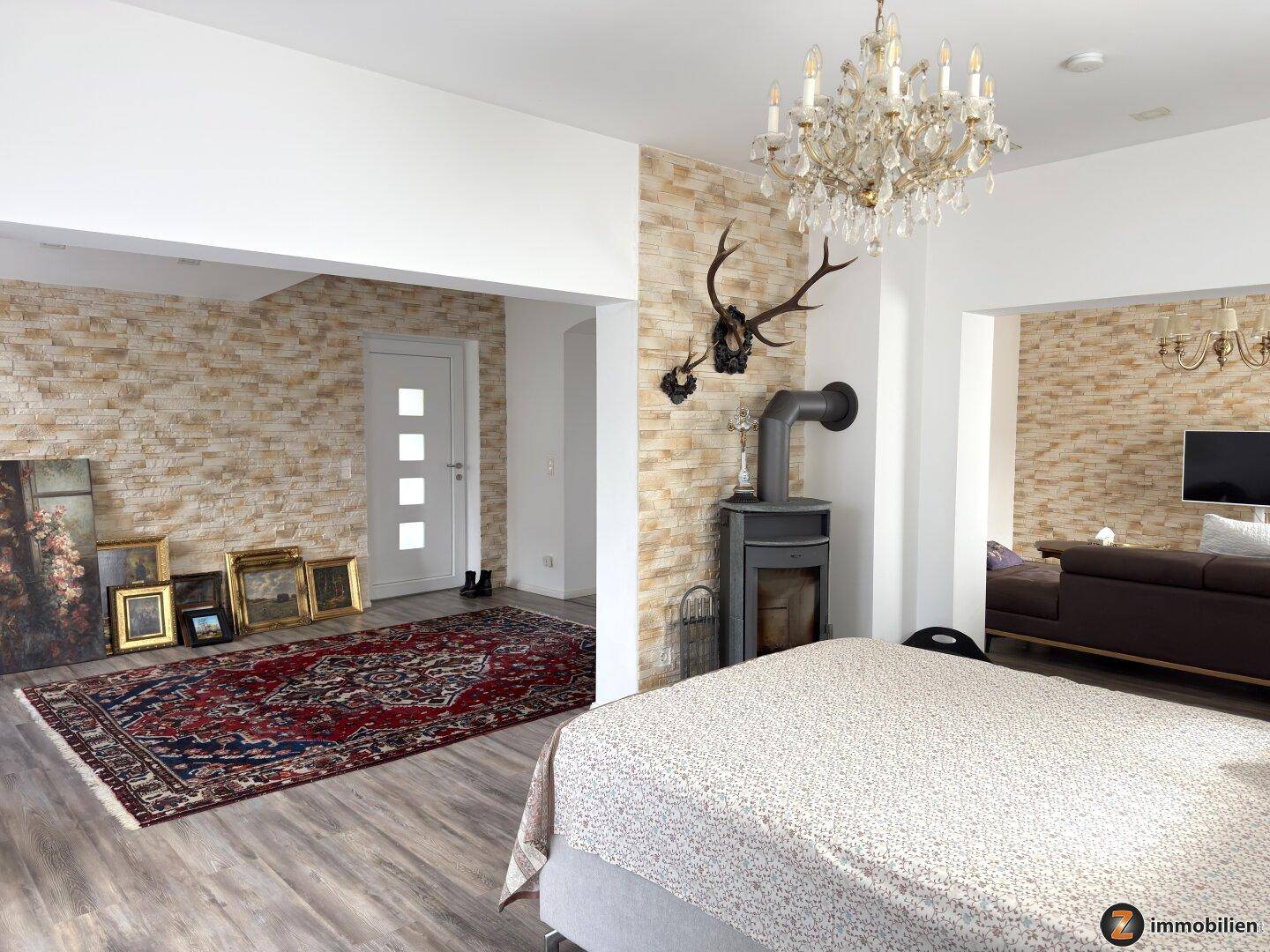 Schlafzimmer mit Kaminofen, dekorativer Steinwand und elegantem Kronleuchter.