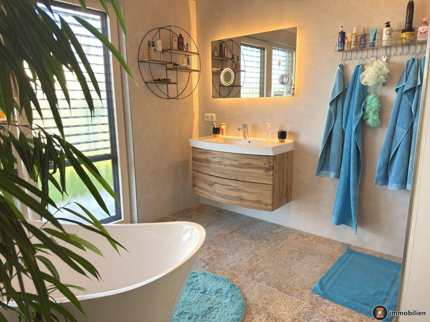 Stilvolles Badezimmer mit modernem Waschtisch, beleuchtetem Spiegel und freistehender Badewanne.