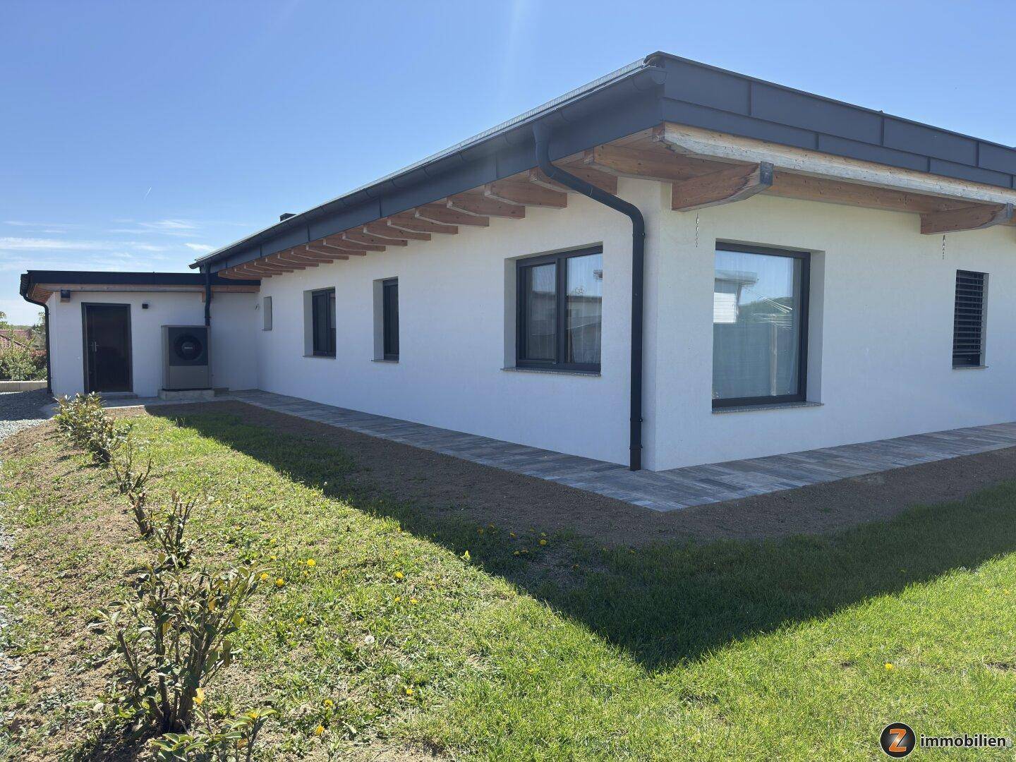 Seitenansicht des modernen Hauses mit Wärmepumpe und gepflegtem Rasenbereich.
