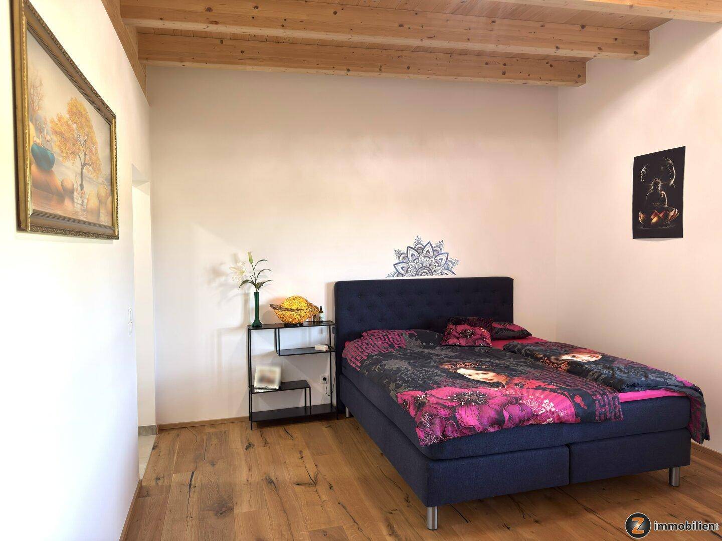 Gemütliches Schlafzimmer mit Holzbalkendecke, Parkettboden und Doppelbett.