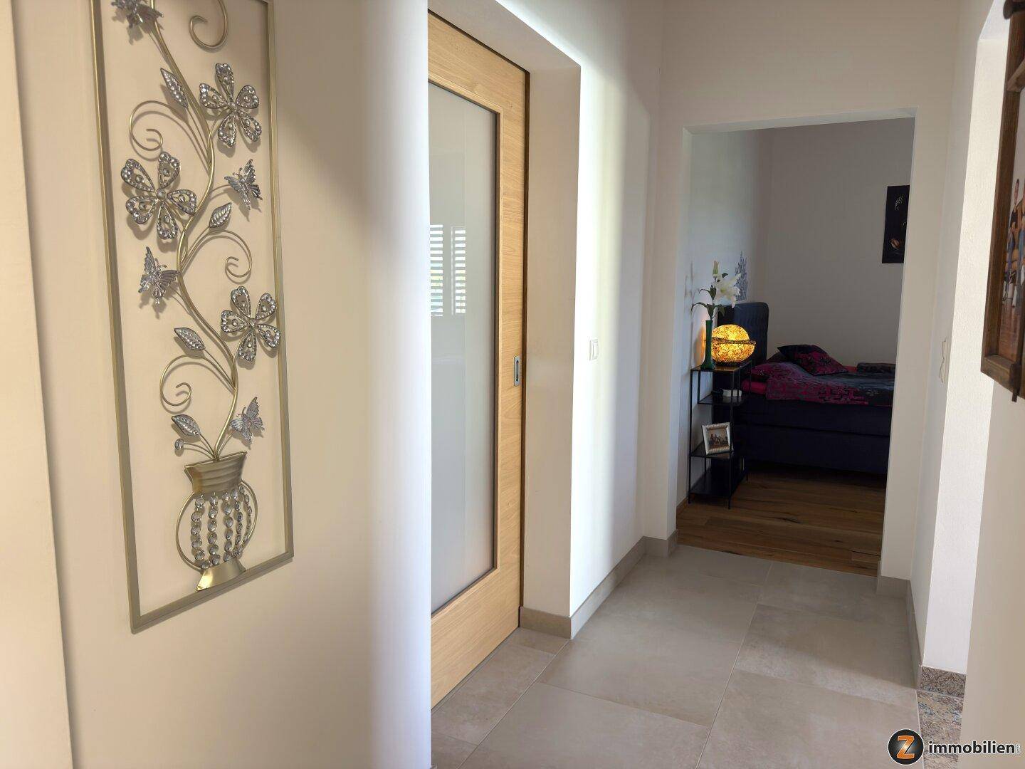 Heller Flur mit Fliesenboden und Blick in ein angrenzendes Schlafzimmer.
