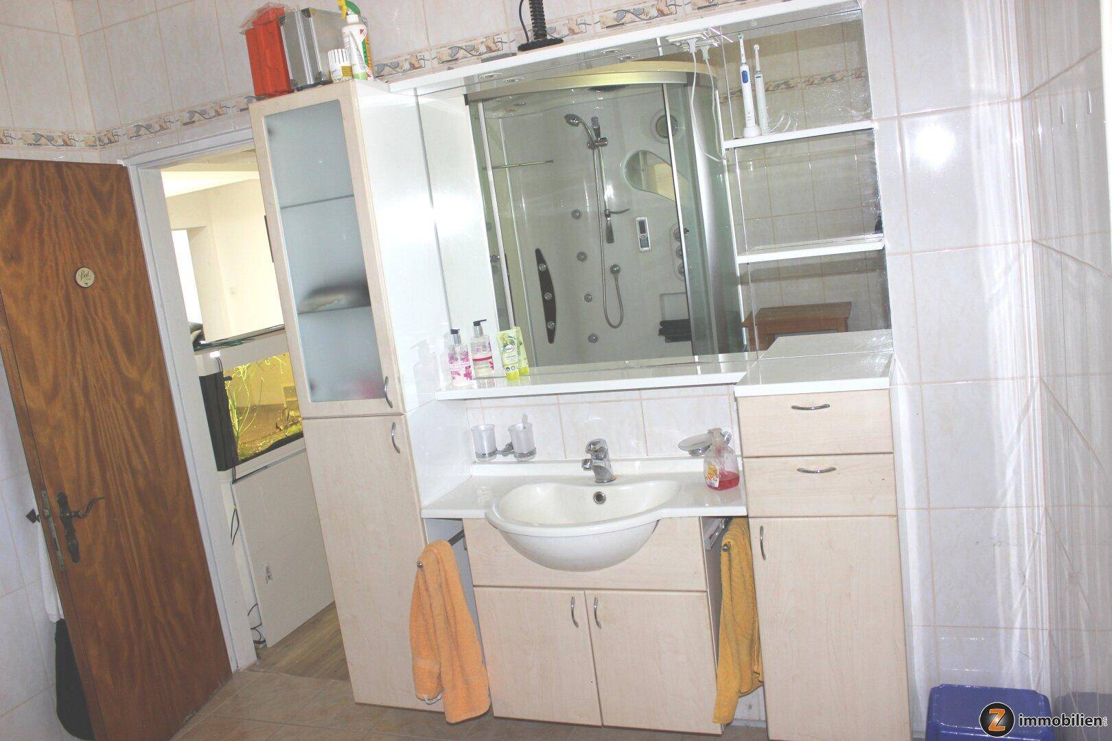 Badezimmer mit Waschtisch, Spiegelschrank und integrierter Duschkabine.