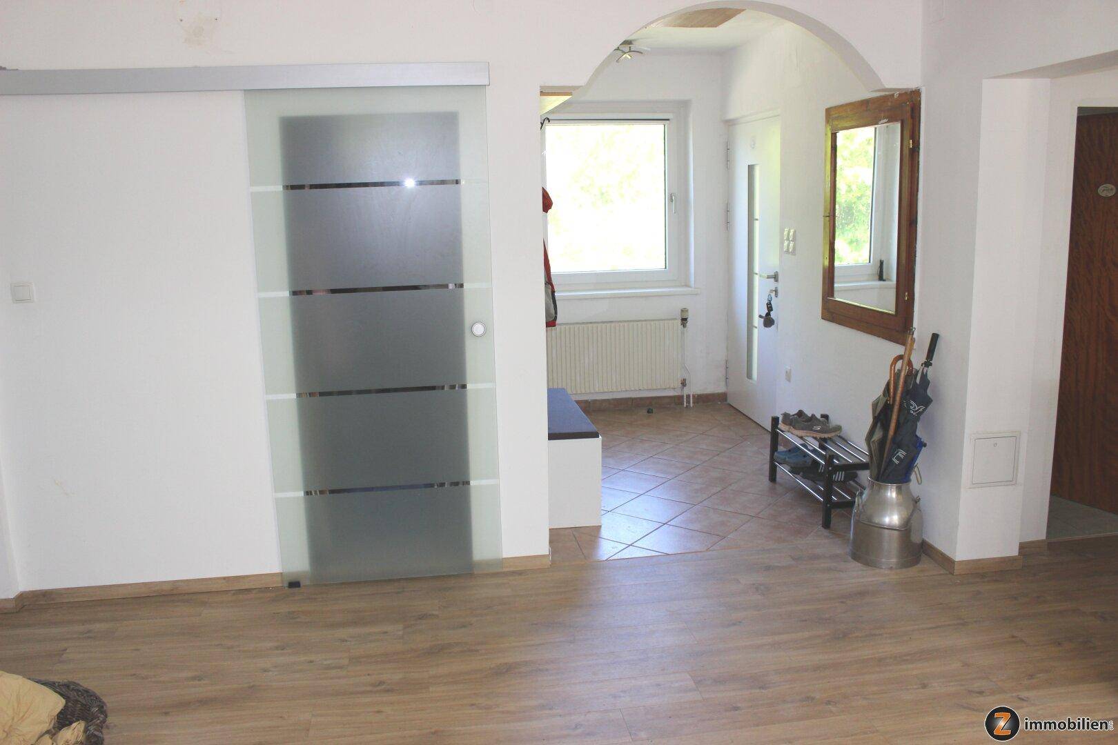 Heller Flur mit Laminatboden, Glasschiebetür und Zugang zu weiteren Räumen.