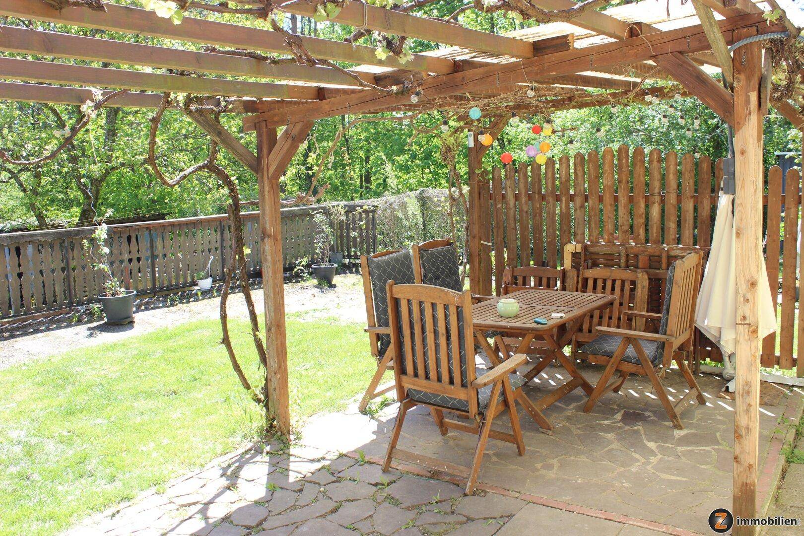 Gemütliche Terrasse unter einer Holzpergola mit Gartenmöbeln und Blick ins Grüne.
