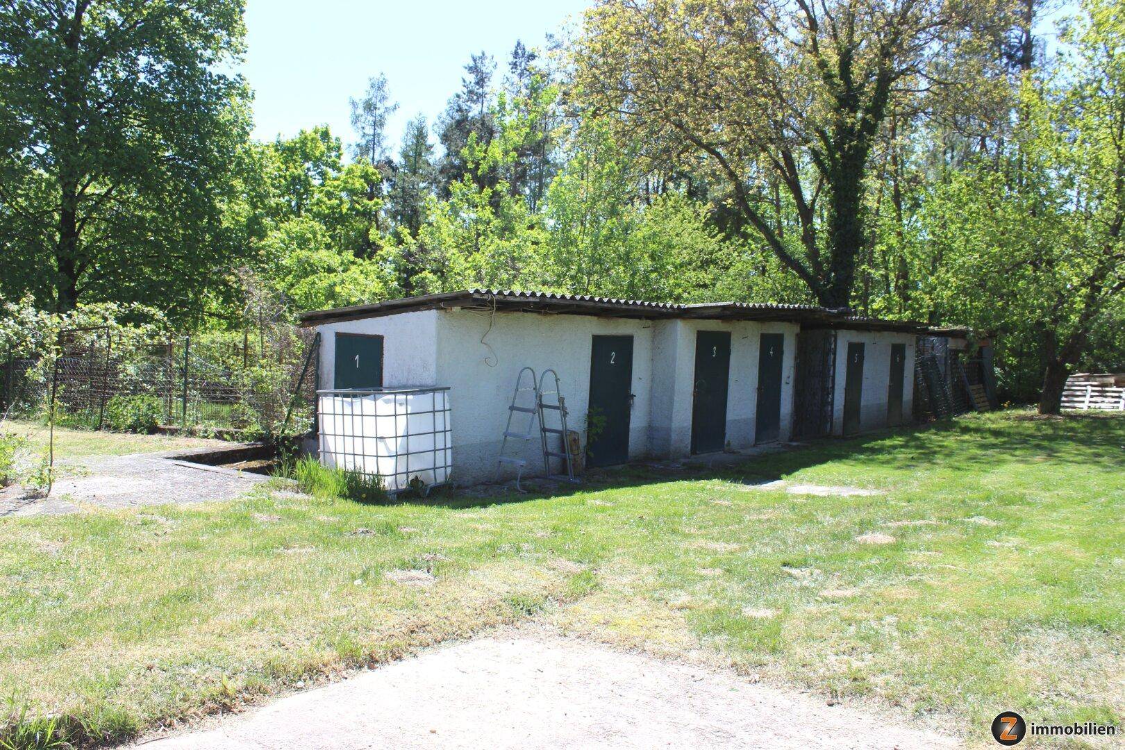 Reihe von einfachen Schuppen oder Nebengebäuden auf einer grünen Wiese.