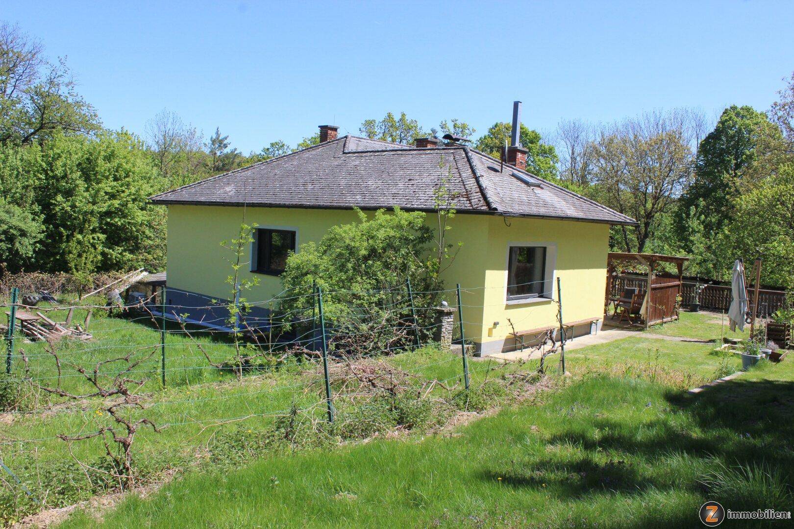 Rückansicht des gelben Hauses mit Gartenbereich und umliegender Natur.