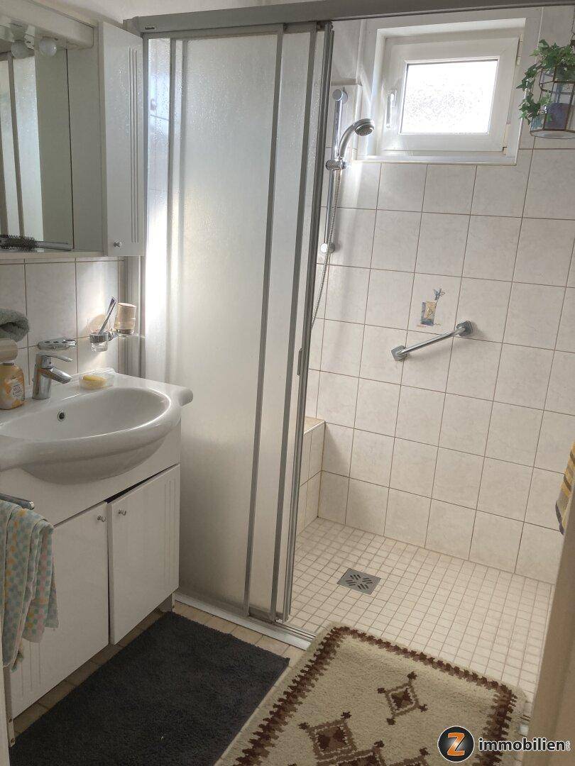 Helles Badezimmer mit Duschkabine, Waschbecken und einem Fenster.
