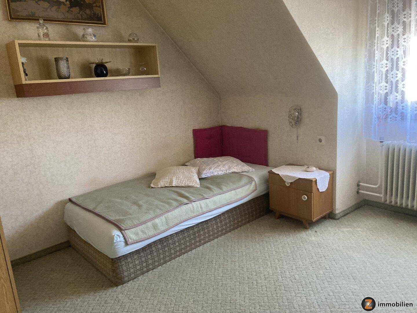 Gemütliches Schlafzimmer im Dachgeschoss mit Einzelbett und schräger Decke.