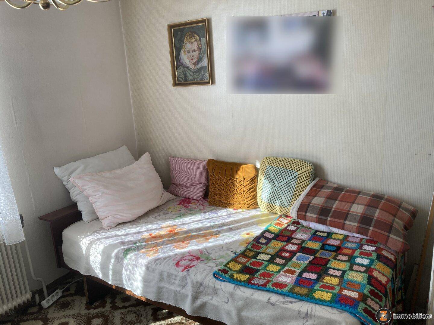 Helles Schlafzimmer mit Einzelbett, bunten Kissen und einfacher Einrichtung.