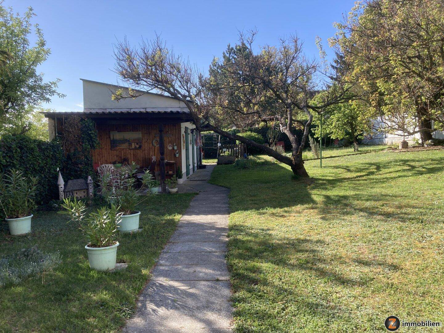 Großer Garten mit Rasenfläche, Bäumen und einem kleinen Gartenhaus im Hintergrund.