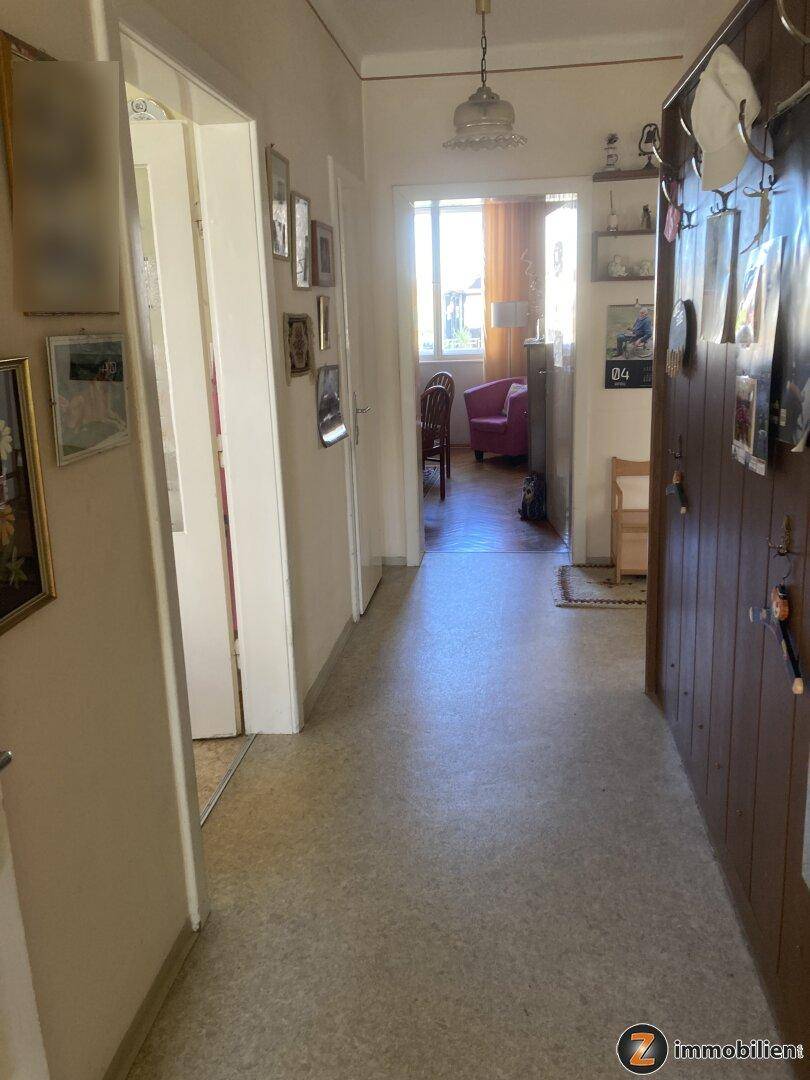 Langer Flur mit hellem Boden, Bildern an der Wand und Blick in einen weiteren Raum.