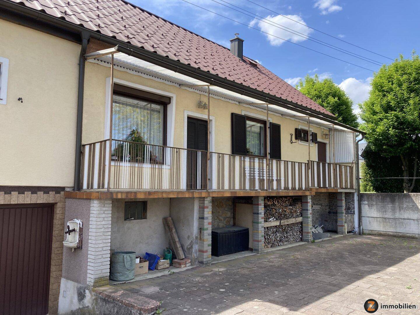 Rückseite des Hauses mit überdachtem Balkon und Holzstapel im Untergeschoss.