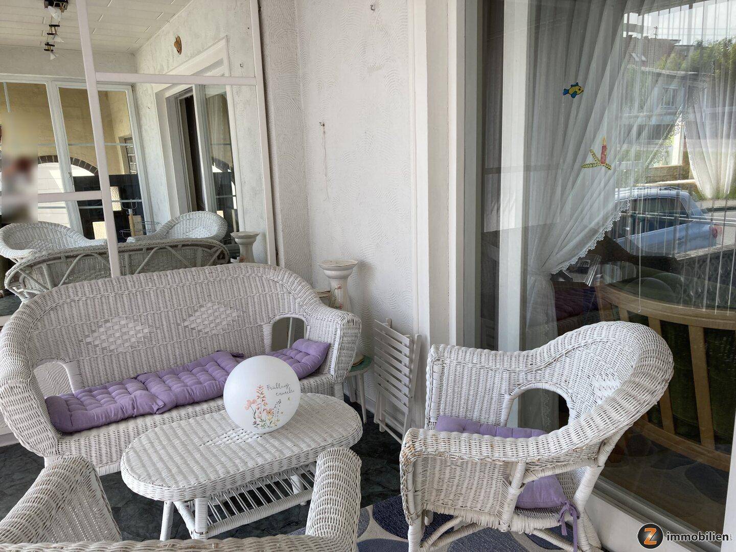 Überdachte Terrasse mit Korbmöbeln und lila Kissen für entspannte Stunden.