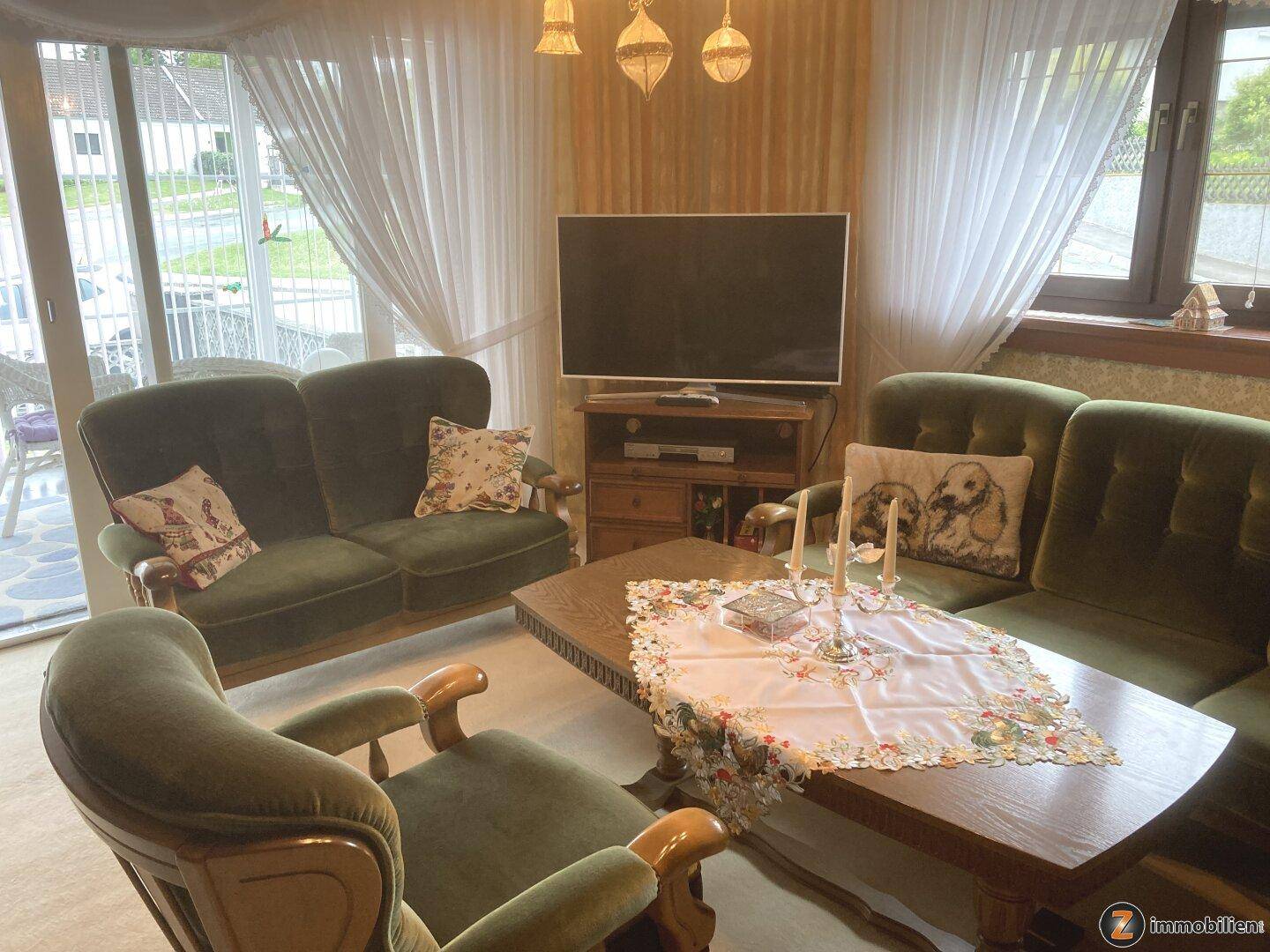 Traditionelles Wohnzimmer mit grünen Samtsofas, Holztisch und Blick nach draußen.