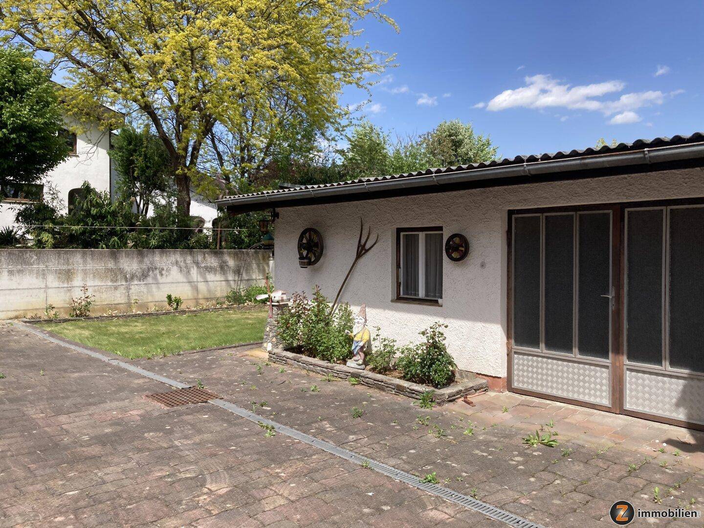 Garage mit gepflastertem Vorplatz und kleinem Gartenbeet.